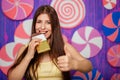 Beautiful woman bites a bar of chocolate on a background of abstract purple wall made of sweets. Royalty Free Stock Photo