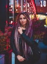 Beautiful woman in black clothes with long pink dreadlocks at night against the background of multicolored lights Royalty Free Stock Photo