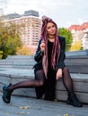 Beautiful woman in black clothes with long pink dreadlocks sits on wooden steps and looks at the camera Royalty Free Stock Photo