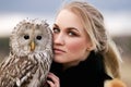 Beautiful woman in a black dress with an owl on his arm. Blonde with long hair in nature holding a owl. Romantic delicate girl Royalty Free Stock Photo