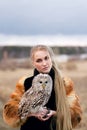 Beautiful woman in a black dress with an owl on his arm. Blonde with long hair in nature holding a owl. Romantic delicate girl