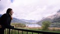 Beautiful woman in a black dress smiling at sunset on a background of mountains and a lake. Laughing girl in a balcony with cloudy Royalty Free Stock Photo