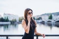 Beautiful woman in black dress standing by a river in city of Prague, making a phone call. Royalty Free Stock Photo