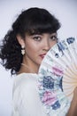 Beautiful woman with black hair and oriental floral fan with earrings and white lace dress modeling portrait