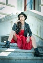 Beautiful woman with black hat, red dress and boots posing sitting on stairs. Young brunette spending time during autumn Royalty Free Stock Photo