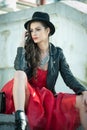 Beautiful woman with black hat, red dress and boots posing sitting on stairs. Young brunette spending time during autumn Royalty Free Stock Photo