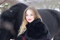 Beautiful woman with a black horse in winter
