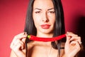 Beautiful woman in black lace lingerie posing in studio with red background. She is playing with chili pepper. Royalty Free Stock Photo