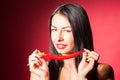 Beautiful woman in black lace lingerie posing in studio with red background. She is playing with chili pepper. Royalty Free Stock Photo