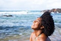 Beautiful woman with black power hair very happy and smiling looking at the camera. Sky clouds rocks and the sea in the background Royalty Free Stock Photo