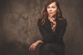 Beautiful woman in black sitting on chair isolated on gray background.