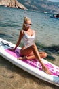 Beautiful woman with blond hair in elegant swimming suit posing with surfer board in the sea