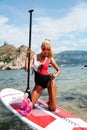 Beautiful woman with blond hair in elegant swimming suit posing with surfer board in the sea