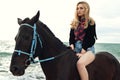 Beautiful woman with blond hair posing with black horse Royalty Free Stock Photo