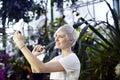 Beautiful woman with blonde short hair taking photo by phone in green park or botanical garden Royalty Free Stock Photo