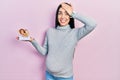 Beautiful woman with blue eyes expecting a baby, holding anatomic fetus stressed and frustrated with hand on head, surprised and Royalty Free Stock Photo