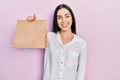 Beautiful woman with blue eyes holding take away paper bag looking positive and happy standing and smiling with a confident smile Royalty Free Stock Photo