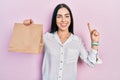 Beautiful woman with blue eyes holding take away paper bag smiling with an idea or question pointing finger with happy face,