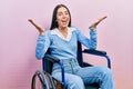 Beautiful woman with blue eyes sitting on wheelchair celebrating crazy and amazed for success with arms raised and open eyes