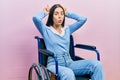 Beautiful woman with blue eyes sitting on wheelchair doing funny gesture with finger over head as bull horns