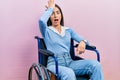 Beautiful woman with blue eyes sitting on wheelchair surprised with hand on head for mistake, remember error