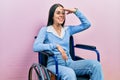 Beautiful woman with blue eyes sitting on wheelchair very happy and smiling looking far away with hand over head Royalty Free Stock Photo