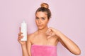 Beautiful woman with blue eyes wearing towel shower after bath holding bottle of body cream with angry face, negative sign showing