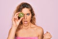 Beautiful woman with blue eyes wearing towel shower after bath holding kiwi fruit over eye annoyed and frustrated shouting with Royalty Free Stock Photo