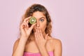 Beautiful woman with blue eyes wearing towel shower after bath holding kiwi fruit over eye cover mouth with hand shocked with Royalty Free Stock Photo