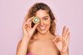 Beautiful woman with blue eyes wearing towel shower after bath holding kiwi fruit over eye doing ok sign with fingers, excellent Royalty Free Stock Photo