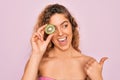 Beautiful woman with blue eyes wearing towel shower after bath holding kiwi fruit over eye pointing and showing with thumb up to Royalty Free Stock Photo