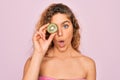 Beautiful woman with blue eyes wearing towel shower after bath holding kiwi fruit over eye scared in shock with a surprise face, Royalty Free Stock Photo