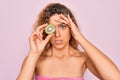 Beautiful woman with blue eyes wearing towel shower after bath holding kiwi fruit over eye stressed with hand on head, shocked Royalty Free Stock Photo