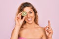 Beautiful woman with blue eyes wearing towel shower after bath holding kiwi fruit over eye surprised with an idea or question Royalty Free Stock Photo