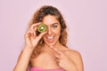 Beautiful woman with blue eyes wearing towel shower after bath holding kiwi fruit over eye very happy pointing with hand and Royalty Free Stock Photo