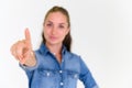 Beautiful woman in blue jeans shirt pointing her finger and looking at camera on white background. Select focus on finger Royalty Free Stock Photo