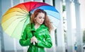 Beautiful woman in bright green coat posing in the rain holding a multicolored umbrella Royalty Free Stock Photo