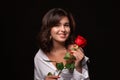 Beautiful woman with bright makeup posing isolated over black background with red rose.
