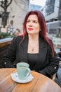 Beautiful woman with bright red lipstick sitting on restaurant terrace. Wonderful woman with red hair in black clothes