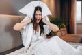 Beautiful woman with brown hair screams while sitting on the bed. Young woman covers her ears with a pillow. Headache Royalty Free Stock Photo