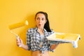 Beautiful woman busy repairing a house, paints the walls yellow with a paint roller,surprised that coped