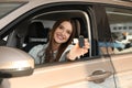 Beautiful woman with car key sitting in auto at dealership Royalty Free Stock Photo