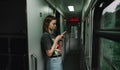 Beautiful woman in casual clothes standing in the train corridor with a smartphone in her hands and enjoys the Internet.lady