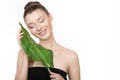 Beautiful woman with clean skin smiling holds a green leaf in her hands.