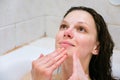 Beautiful woman cleaning her face with a foam treatment on white bath Royalty Free Stock Photo