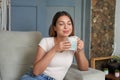 Beautiful woman with closed eyes holding a mug of hot drink sitting relaxed on couch at home Royalty Free Stock Photo