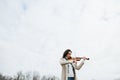 Beautiful woman in a coat playing violin under a sky with her eyes closed