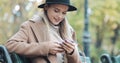 Beautiful woman in coat using smartphone relaxes on the bench in autumn park. Technology outdoors Royalty Free Stock Photo
