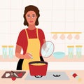 Beautiful woman cooking in her kitchen. brunette in a red dress and yellow apron salt soup and holds the lid from the