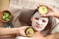 Beautiful woman with cotton mask sheet on face and cut avocado relaxing in spa salon Royalty Free Stock Photo